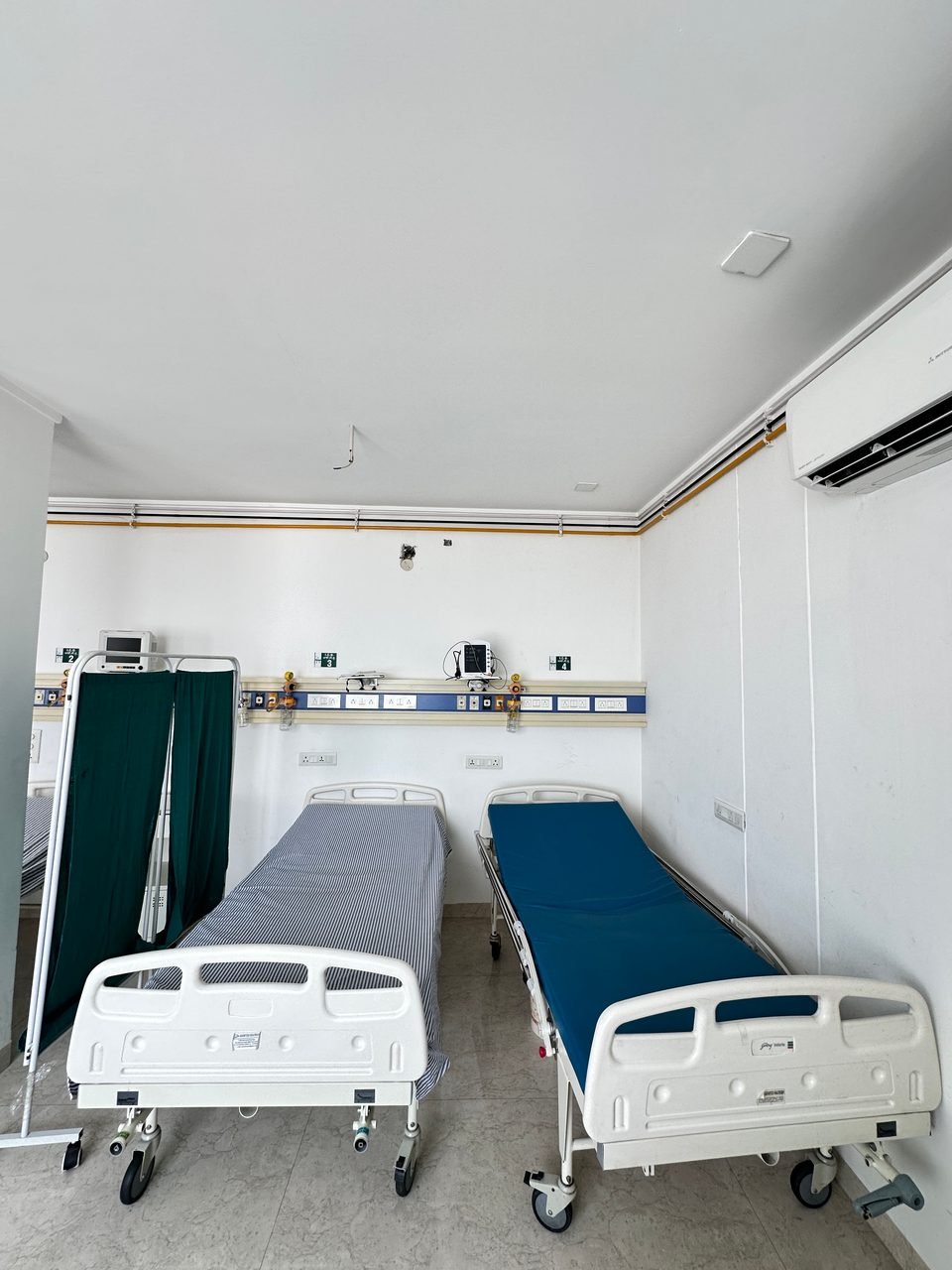 Two hospital beds with a green privacy screen and wall monitors